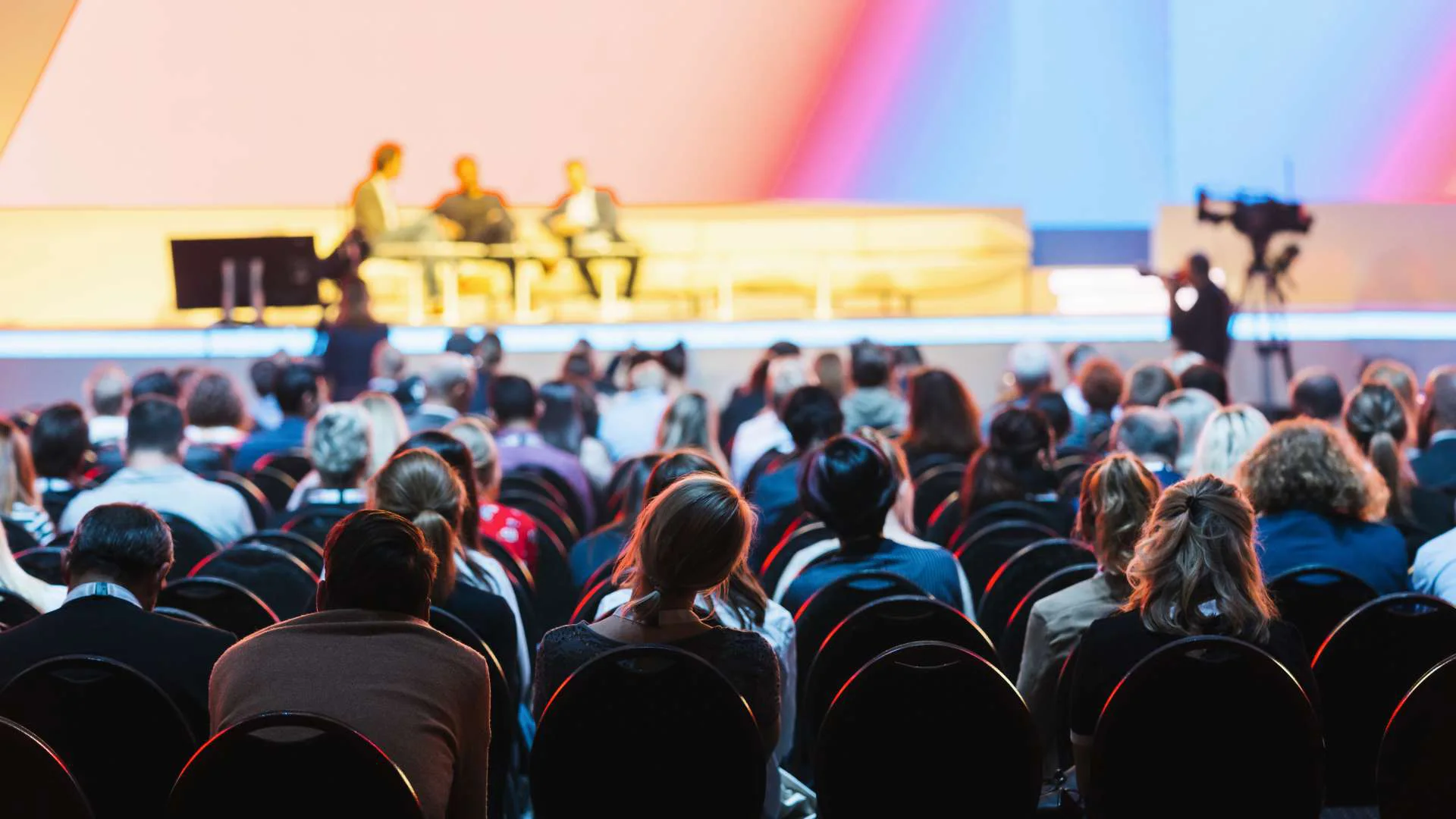 A three-person panel on stage in front of a seated crowd